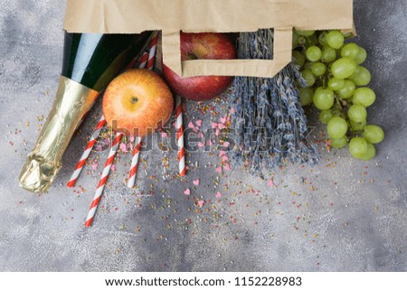 Wine, fruits, flowers (set for the party or picnic) in a paper craft pack on a gray concrete background. Top view. Copy space below. Festive, joyful mood