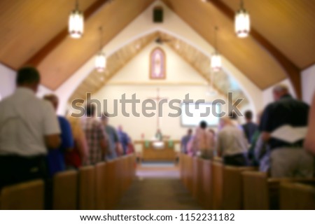 A blurred photo of the inside of a church sanctuary that is filled with people in the pews, and the pastor stands under a large cross at the altar. Royalty-Free Stock Photo #1152231182