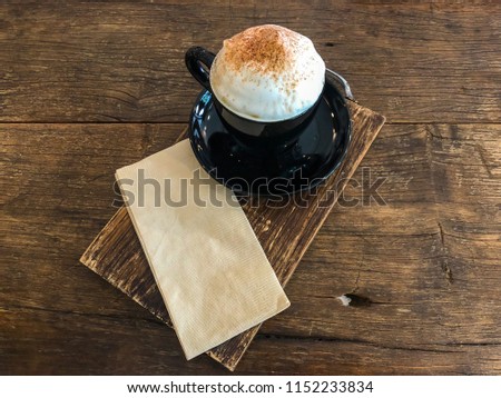 Hot coffee with milk foam. In black coffee mug Put on wooden board Put on wooden board. Available space for adding text.