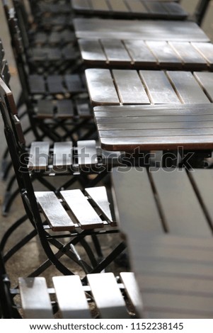 Close up outdoor view of pattern of tables and metallic chairs with wooden seats. Furnitures located outside, in front of a restaurant. Abstract design with lines and planks lighted by the sun. 