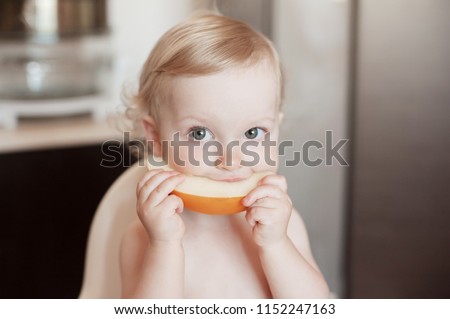Baby girl eating Honeydew Melon. Funny  laughing child in the kitchen. Сheerful kid in the high chair