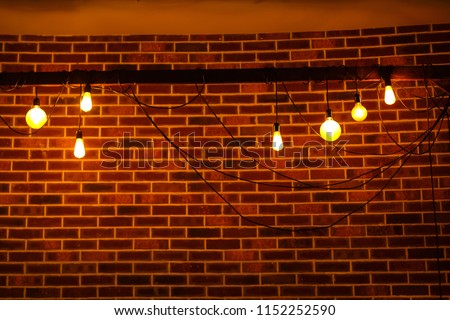 A lot of yellow incandescent light bulbs hang on the background of a black brick wall. Garland