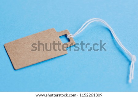 Blank brown cardboard price tag, sale tag, gift tag, address label, luggage label on blue background. Mock up, copy space for text, side view