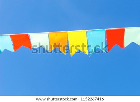 Multicolored flags a triangular shape  against the blue sky. Good background on the theme of a city street holiday