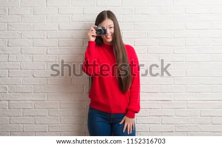Young Chinese woman over brick wall holding vintage camera with a happy face standing and smiling with a confident smile showing teeth