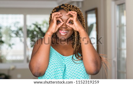 African american woman at home doing ok gesture like binoculars sticking tongue out, eyes looking through fingers. Crazy expression.