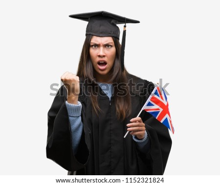 Young hispanic woman wearing graduated uniform holding flag of united kingdom annoyed and frustrated shouting with anger, crazy and yelling with raised hand, anger concept