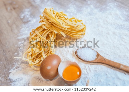 Raw tagliatelle nido on the flour-dusted wooden background. Making Fresh Pasta Tagliatelle from a Traditional Pasta Machine. Italian foods concept and menu design.