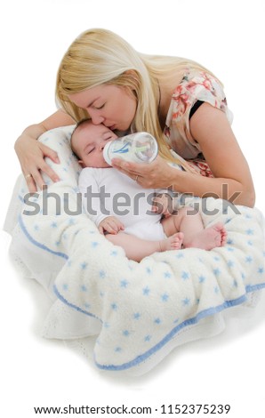The concept of caring for the baby. Mother feeding baby with milk from a bottle on the baby chair, kissing him on the cheek. Isolated on white background

