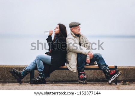 A girl on rollers drinks water from a bottle. Father and daughter on roller skates sit on a bench. Sport and water. Active old people in retirement.