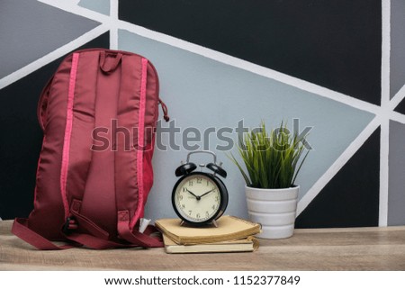 the concept of school bag equipment, books, alarm clocks and ornamental plants on the table.