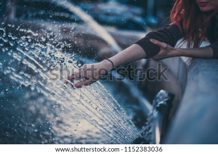 Closeup photo of woman hand touches clean and fresh water from the fountain. Water splashes all around.