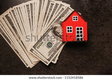 Red wooden house model over pile of money isolated on table background. Home money concept and free copy space.
