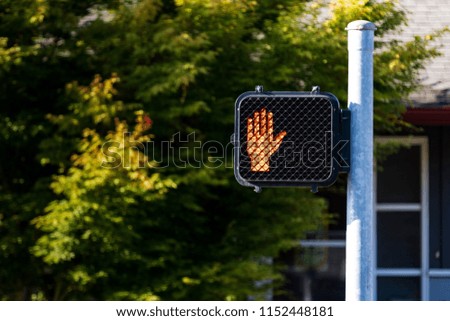 Crosswalk hand symbol sign on a post with trees in the distance