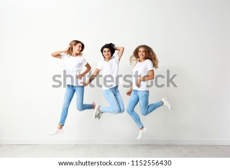 Group of young women in jeans jumping near light wall