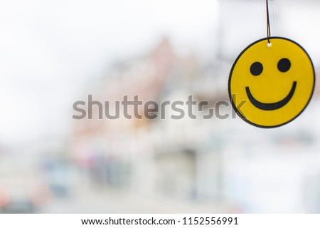 Happy Face Car Air Freshener with large copy space on the left yellow and black smiling face hanging with a blurred white and mixed colour background
