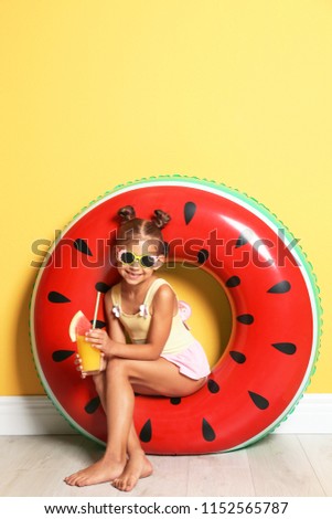 Cute little girl with inflatable ring and glass of cocktail near color wall
