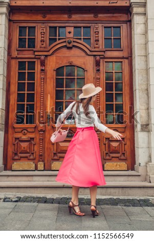 Young woman wearing stylish clothing and accessories outdoors. Model dancing against old wooden door on city street. Beauty fashion concept