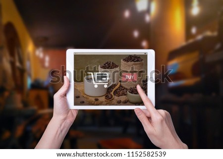 Shopping online concep, Hand using mock up computer tablet, with picture hot cup of coffee with beans on burlap sack  on coffee shop cafe background, and copy space