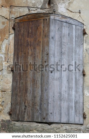 Close up front view of an ancient window with closed wooden shutters. Detail of an ancient facade in a french street. Vintage image with weathered planks and stone wall. Abstract architectural picture