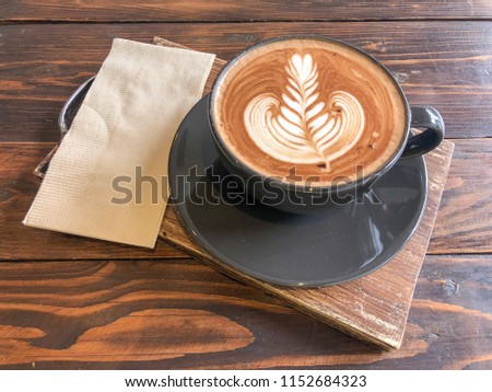 Hot Mocha Latte Coffee decorated with latte art. In black coffee mug Put on wooden board Put on wooden board. Available space for adding text.