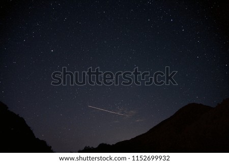 Meteors in the pure starry night sky above the mountain river. Bright multicolored stars of the Milky Way overhead. A huge universe.