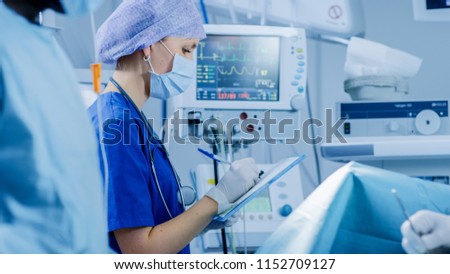 In the Hospital Operating Room Anesthesiologist Looks and Monitors and Controls Patient's Vital Signs, Nodding to a Chief Surgeon to Proceed with Surgery.