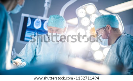 Low Angle Shot in the Operating Room, Assistant Hands out Instruments to Surgeons During Operation. Surgeons Perform Operation. Professional Medical Doctors Performing Surgery. Royalty-Free Stock Photo #1152711494