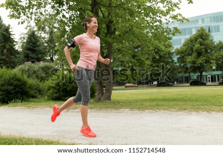 fitness, sport and healthy lifestyle concept - smiling woman with earphones wearing armband with smartphone and jogging at park and listening to music