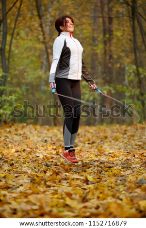 Picture of side view of sports girl jumping rope at autumn forest