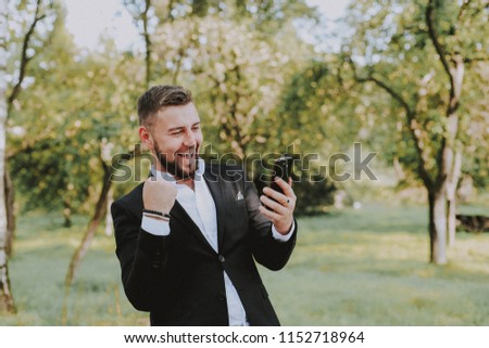 A businessman in his glasses holds the phone in his hands and rejoices in victory
