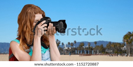 travel, tourism and photography concept - happy young woman with backpack and camera photographing over venice beach background in california