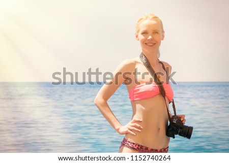 A female photographer in a swimsuit makes a photo on the sea, the ocean. Beach vacation, travel.