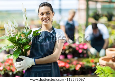 happy female nursery owner with pot of flowers inside greenhouse Royalty-Free Stock Photo #115275067