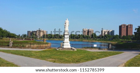 View of Druid Hill Park  (Baltimore, MD).  Statue of Christopher Columbus.  View of reservoir.  Tall, residential buildings across the street from the park.  Clear, blue sky.