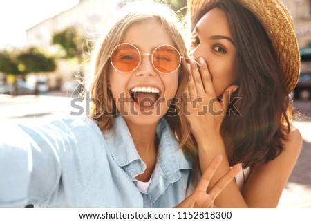 Portrait of two pretty cute teenagers blond and brunette models share secrets, gossip. Surprise face, emotions, Best friends wearing stylish outfit and taking selfie on the street background