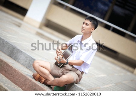 Thai boy in Thai student uniform (brown/khaki shorts), playing a guitar