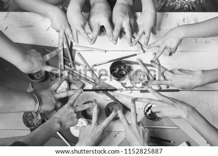 Messy art concept. Artists hands with stationery and colored paper. Hands show victory signs above markers, pencils and paints. Art supplies near big and small hands on white background, top view