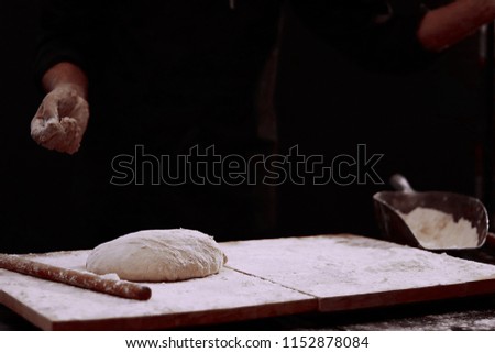 Man baking bread. Sprinkling some flour on dough. Hands kneading dough.  Male chef prepares a meal of flour. 