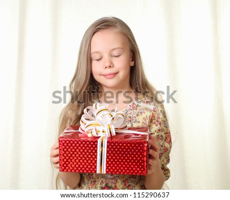 Little blond girl holding a red glamorous gift and looking on it