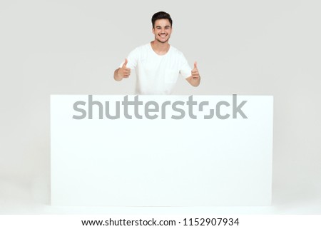 Handsome guy posing with blank white banner, signboard, isolated on white studio background. Happy man looking at camera.