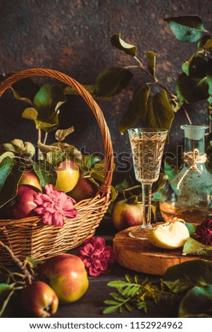 Apple cider in a glass and a decanter and basket with ripe apples on a wooden table in vintage style