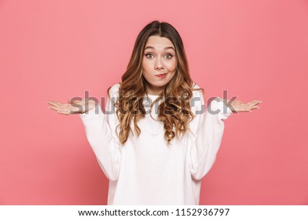 Portrait of a confused young casual girl shrugging shoulders isolated over pink background Royalty-Free Stock Photo #1152936797
