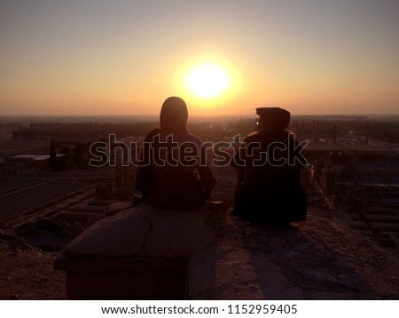 Silhouettes of two lovers sitting together on the top of mountains talking and looking at a beautiful sunset over Persepolis, Iran