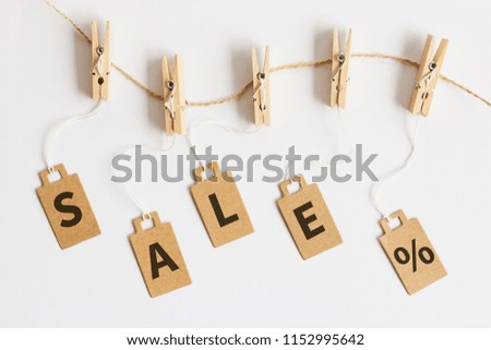 Brown cardboard price tags with sign sale hanging on wooden clothes clips on white background, top view