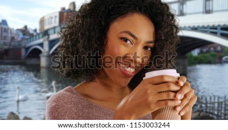 Happy young black woman tourist drinking tea in Windsor out of paper to go cup