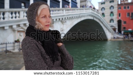 Mature woman in sweater and scarf looking out over canal on venice vacation