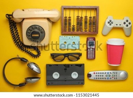 Retro objects on a yellow background. Rotary telephone, audio cassette, video cassette, gamepad, 3d glasses, tv remote, headphones, push-button phone. Analog media technology of the past. Flat lay.
