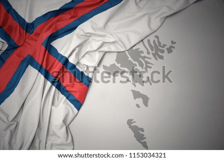 waving colorful national flag of faroe islands on a gray map background.