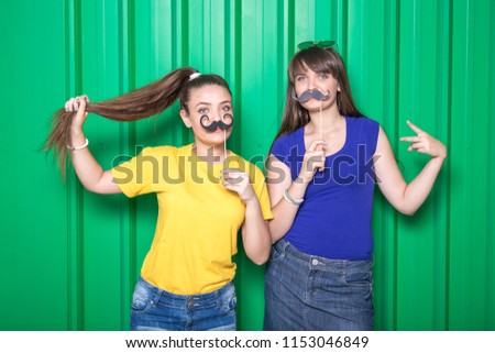 Portrait of two girls with mustache paper props on green background.